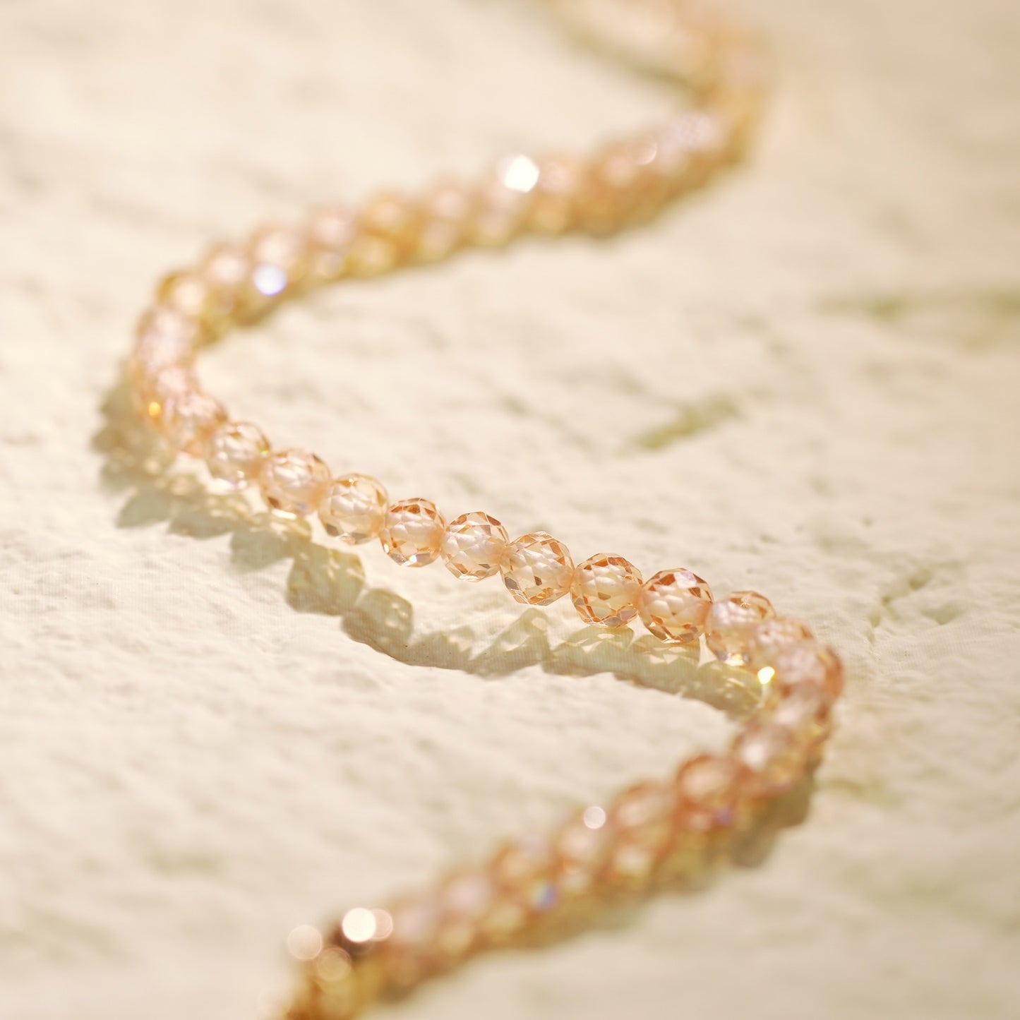 Close-up of the Champagne Light Necklace arranged in a spiral, highlighting the shimmer of CZ beads and gold accents in a clean, modern design.