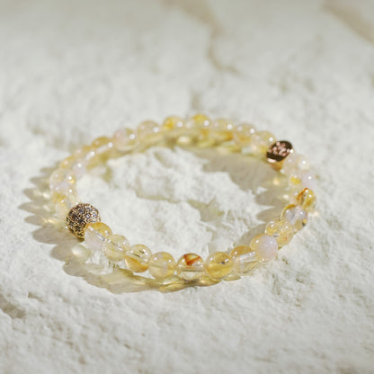 A stretch bracelet made with golden-yellow citrine beads, a gold-plated CZ bead, and a Gina Kim logo charm. Bright, joyful, and handmade.