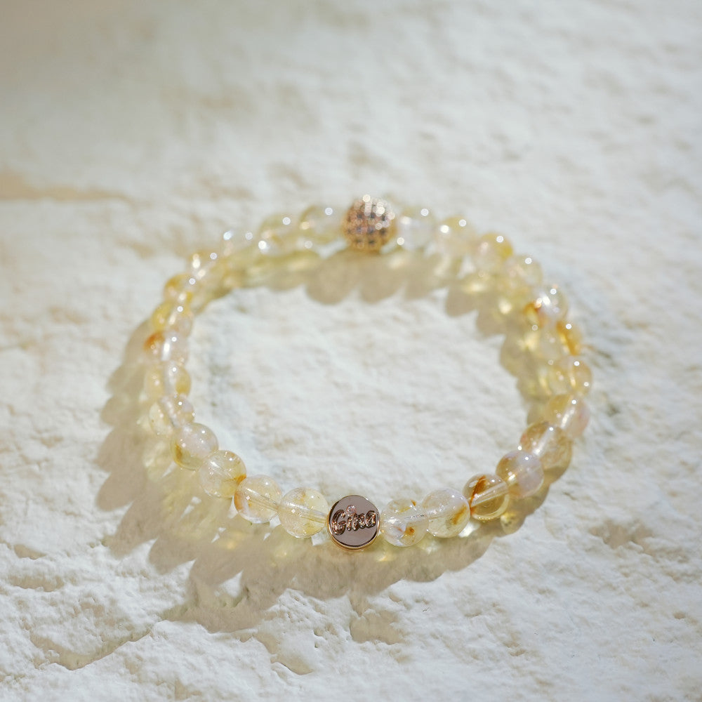 A stretch bracelet made with golden-yellow citrine beads, a gold-plated CZ bead, and a Gina Kim logo charm. Bright, joyful, and handmade.