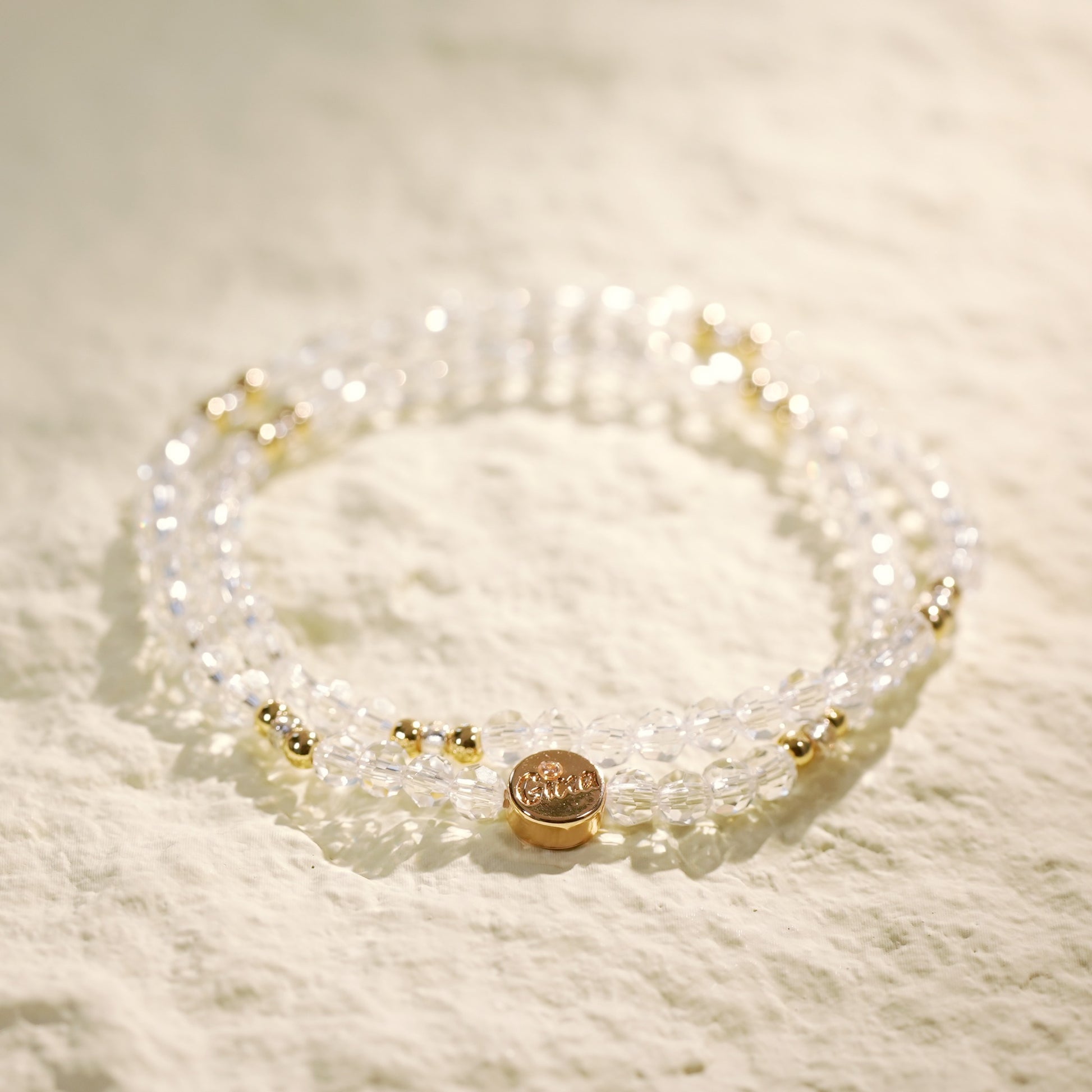 A double-row crystal quartz stretch bracelet with gold-toned accents and a Gina Kim logo tag. Clean, elegant, and handmade.