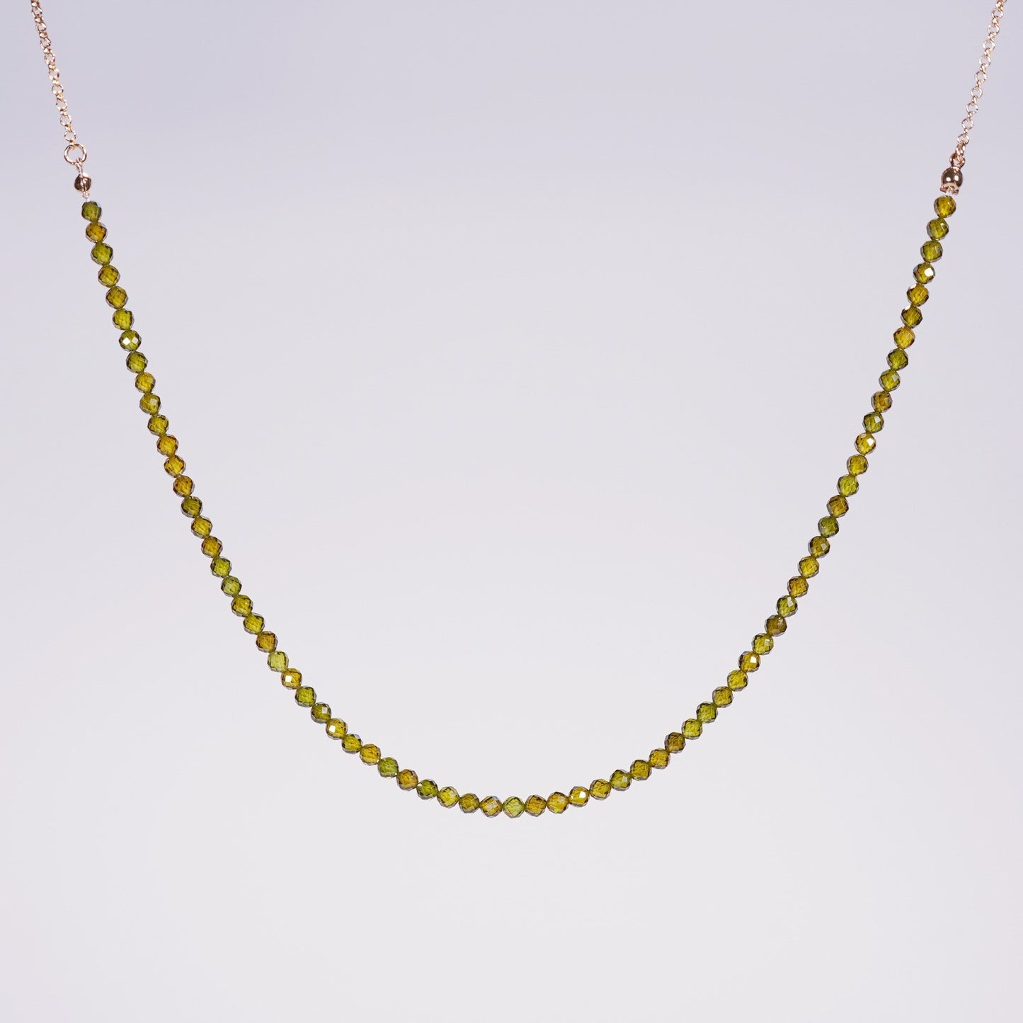 Flat-lay of the Forest Light Necklace showing deep green CZ beads and gold accents, styled for minimalist elegance on a neutral satin background.