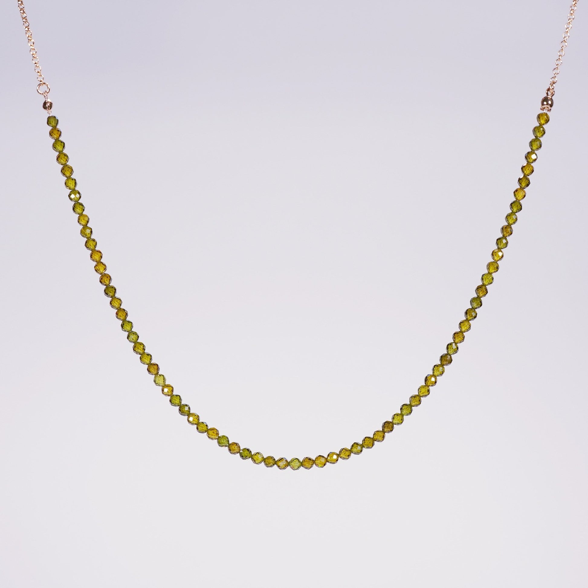 Flat-lay of the Forest Light Necklace showing deep green CZ beads and gold accents, styled for minimalist elegance on a neutral satin background.