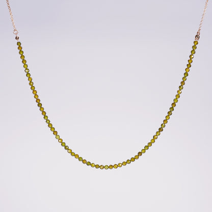 Flat-lay of the Forest Light Necklace showing deep green CZ beads and gold accents, styled for minimalist elegance on a neutral satin background.