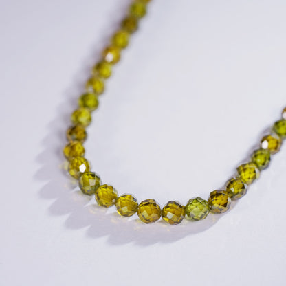 Close-up of the Forest Light Necklace in a U-shaped arrangement, showing deep green faceted CZ beads and gold accents. Displayed on a neutral background to emphasize color contrast.