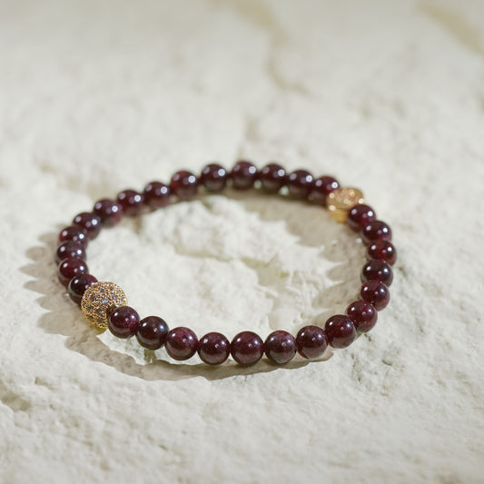 A stretch bracelet with rich red garnet beads, a gold-plated CZ bead, and a Gina Kim logo charm. Bold, elegant, and handmade.