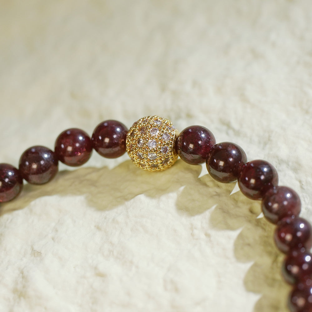A stretch bracelet with rich red garnet beads, a gold-plated CZ bead, and a Gina Kim logo charm. Bold, elegant, and handmade.