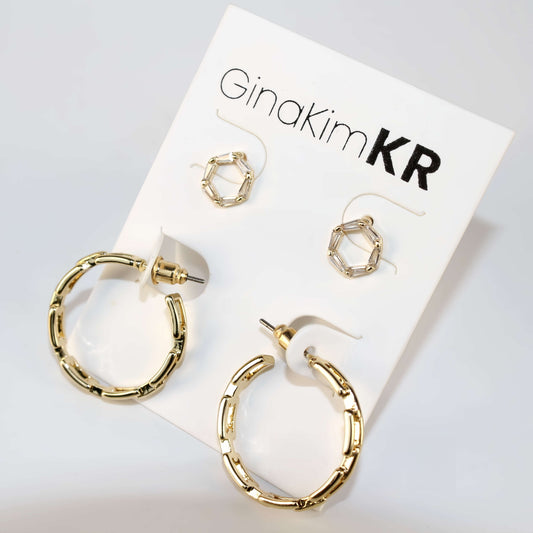 Geo Spark Earring Set laid out with visible reflections, showcasing 8mm CZ studs and 24mm gold hoops with decorative cut-outs in soft lighting.
