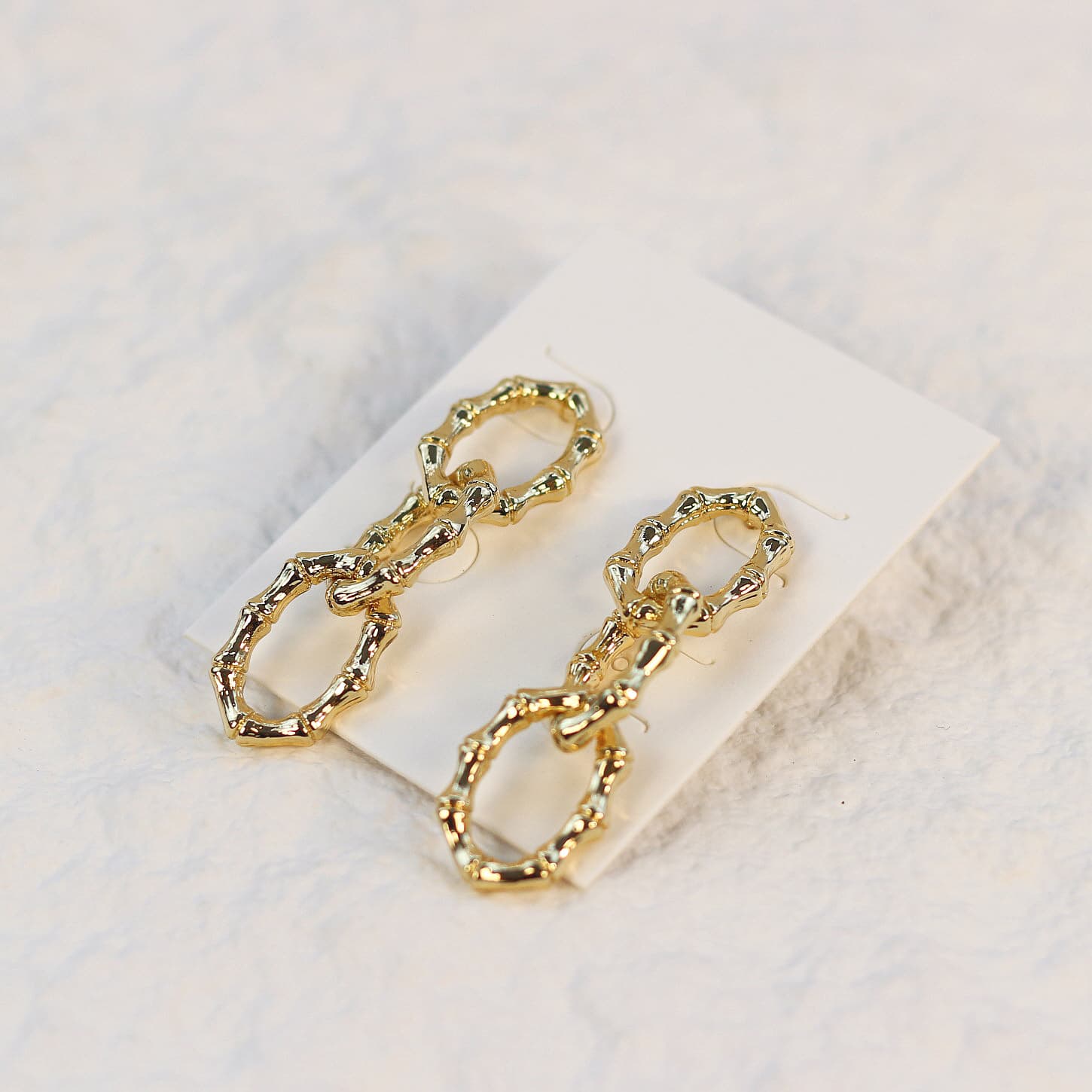 Angled shot of Bamboo Link Drop Earrings showing gold oval links with a polished bamboo finish on a soft cream-colored card.