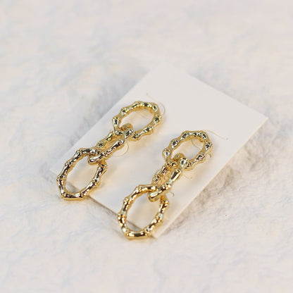 Angled shot of Bamboo Link Drop Earrings showing gold oval links with a polished bamboo finish on a soft cream-colored card.
