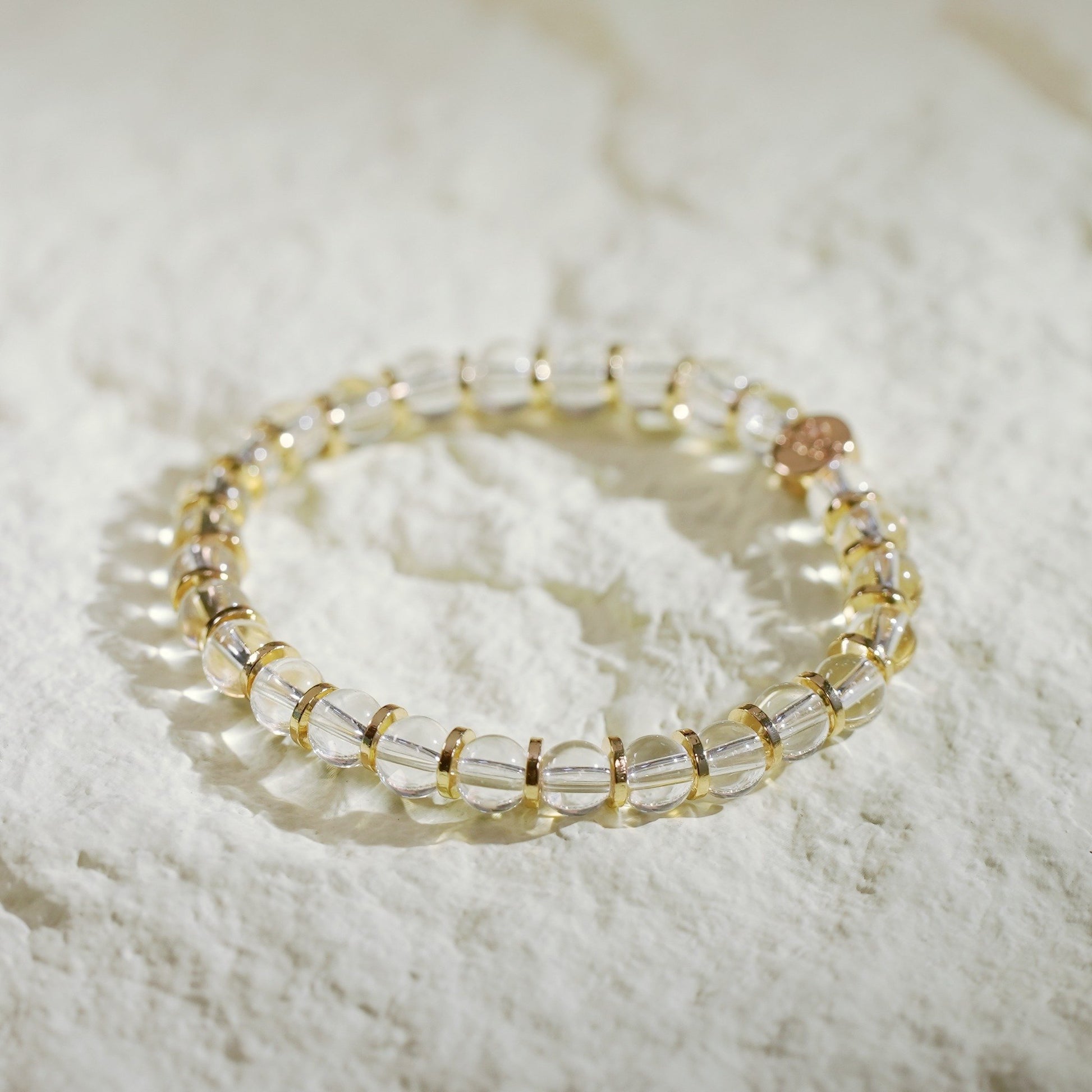 A crystal quartz stretch bracelet with gold-toned spacers, designed for clarity and elegance. Handmade by Gina Kim Jewelry