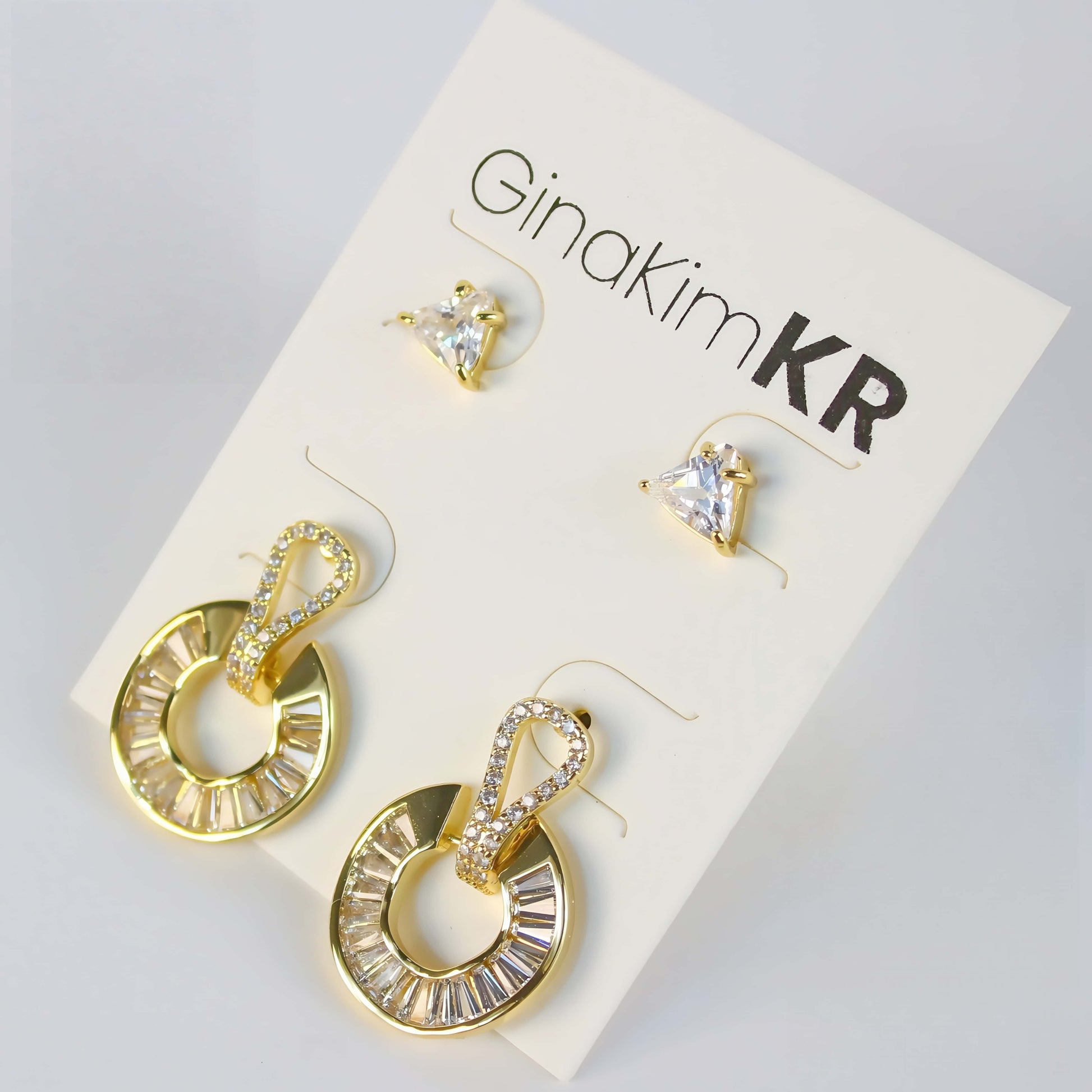 Golden Edge Duo by GinaKimKR – Elegant 2-pair earring set with triangle CZ studs and baguette crystal gold loop drops, shown on brand card