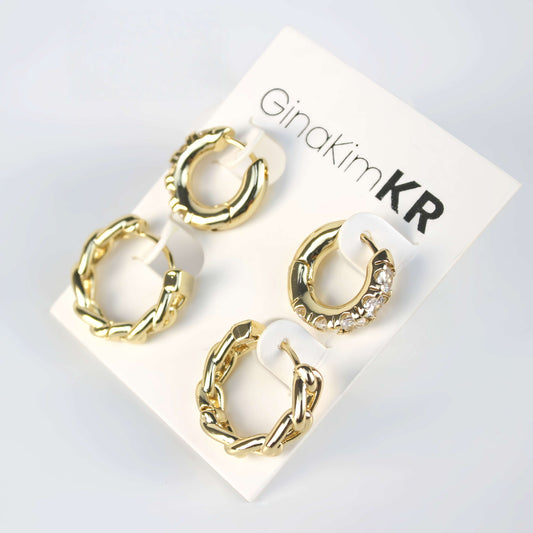Four-piece gold huggie earring set with twisted and crystal-studded designs on GinaKimKR card, photographed in soft natural light