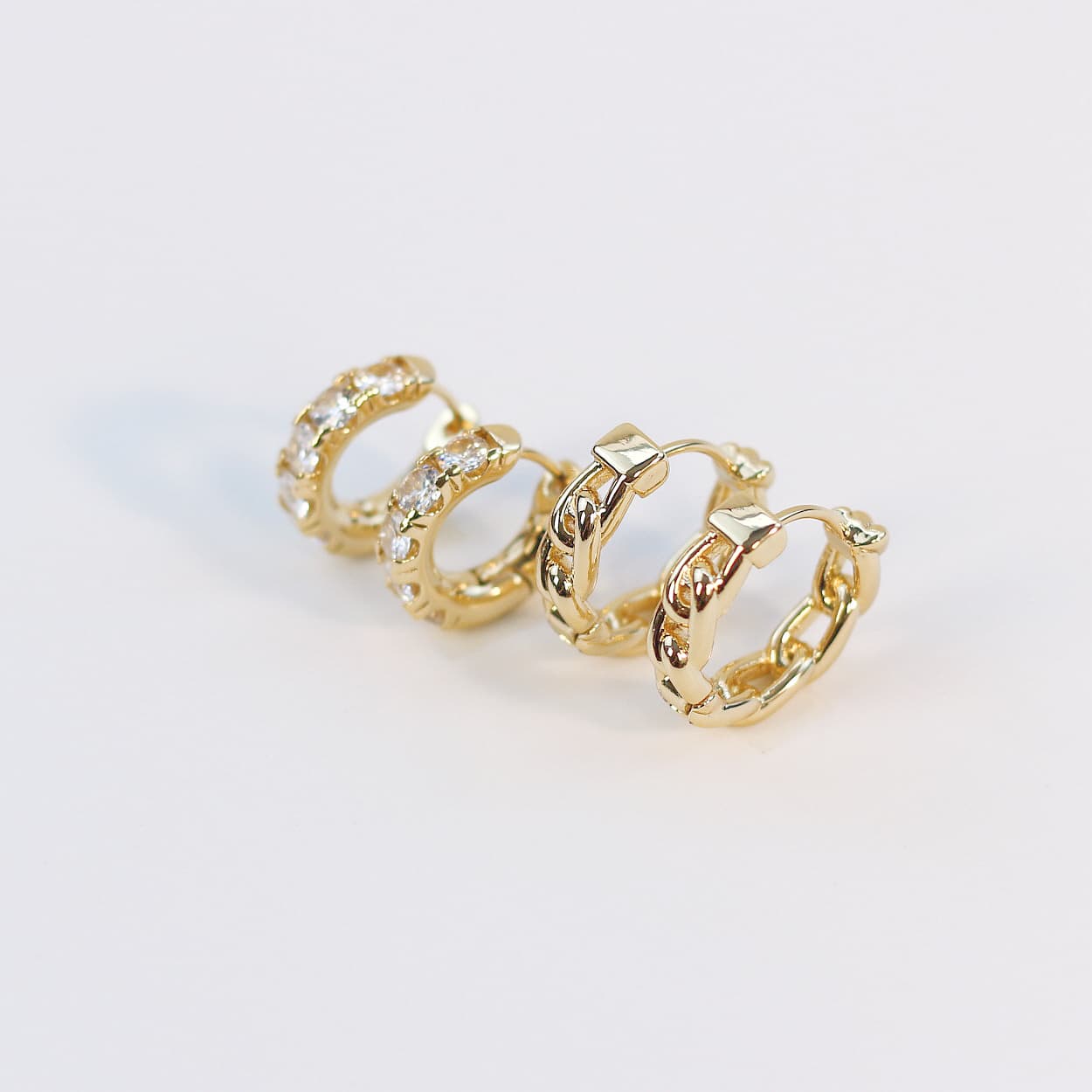 Angled close-up of four gold huggie earrings from the Golden Gleam Set, emphasizing texture and crystal shine on a white display card.