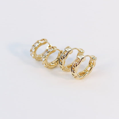 Angled close-up of four gold huggie earrings from the Golden Gleam Set, emphasizing texture and crystal shine on a white display card.