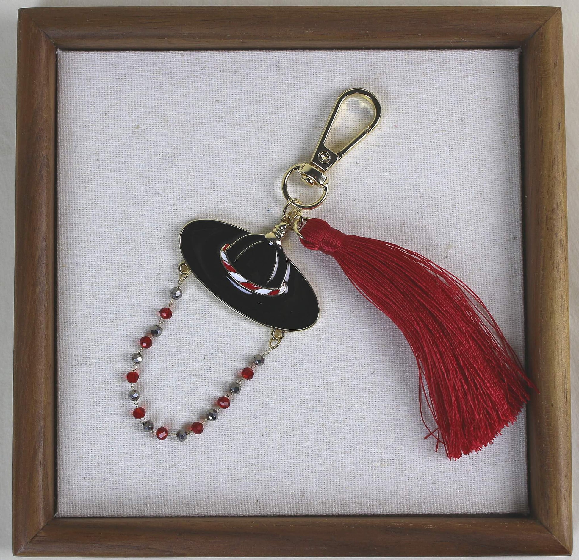 Joseon Crimson Guardian Key Ring displayed in a wooden frame showing the Korean Satto hat motif with a bold crimson tassel.