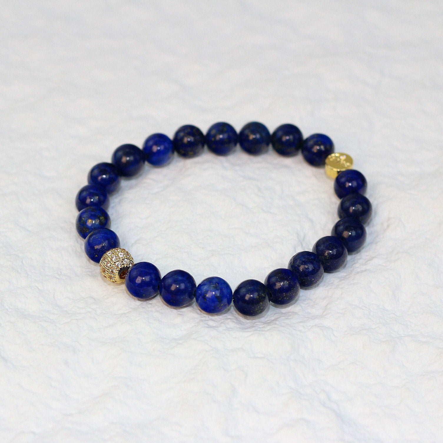 Top-down view of the Lapis Strength Bracelet featuring deep navy 8mm round beads with natural flecks of gold, arranged on a white background.