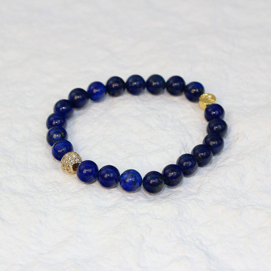 Top-down view of the Lapis Strength Bracelet featuring deep navy 8mm round beads with natural flecks of gold, arranged on a white background.