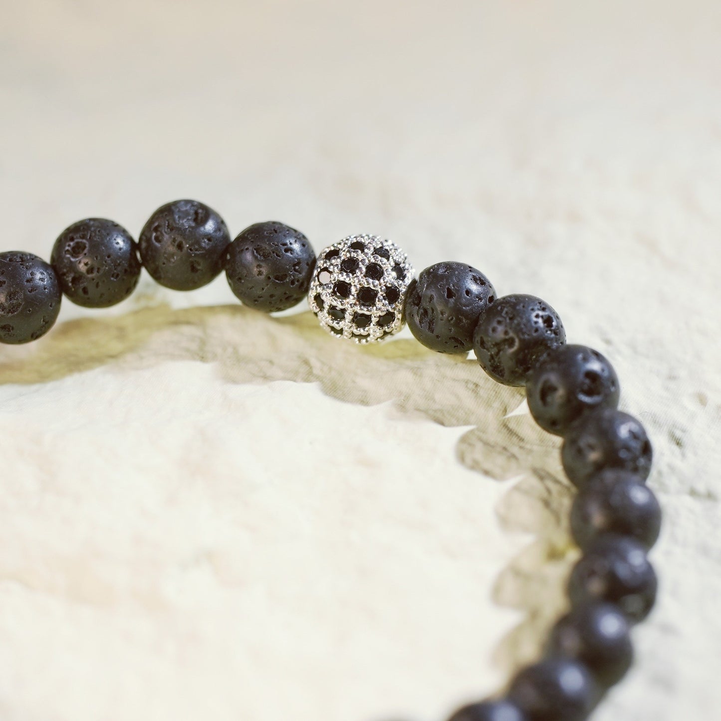 A natural lava stone stretch bracelet with silver accents and a Gina Kim logo charm. Bold, grounding, and handmade
