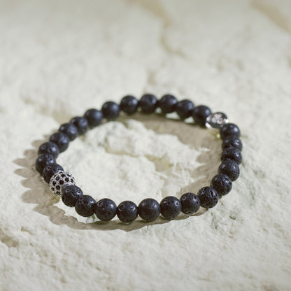 A natural lava stone stretch bracelet with silver accents and a Gina Kim logo charm. Bold, grounding, and handmade