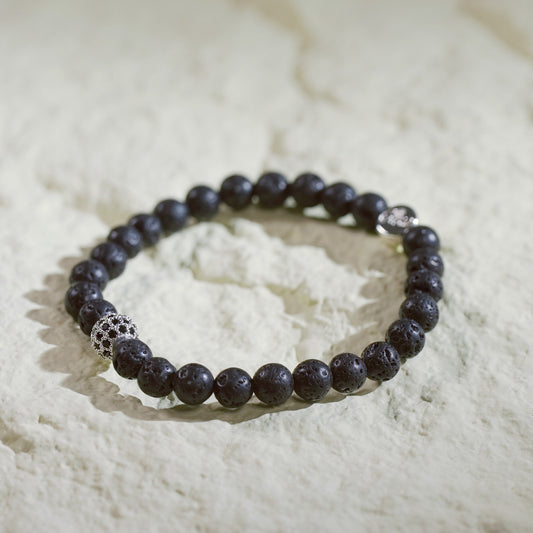 A natural lava stone stretch bracelet with silver accents and a Gina Kim logo charm. Bold, grounding, and handmade