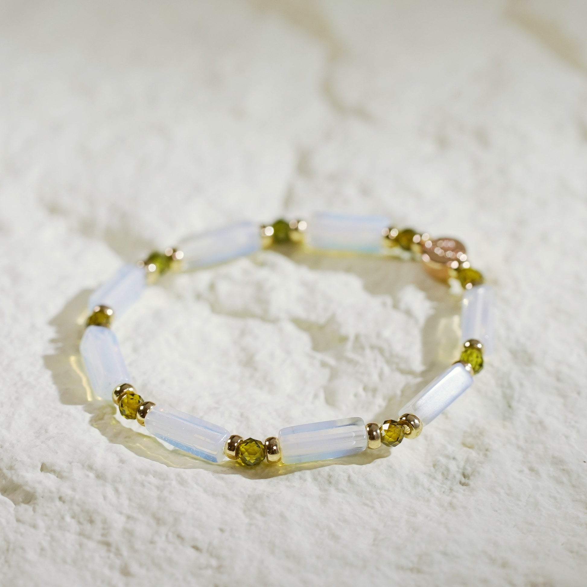 A unisex moonstone stretch bracelet with rectangular beads, deep green CZ accents, and gold-toned details. Designed by Gina Kim, symbolizing calm and quiet luxury