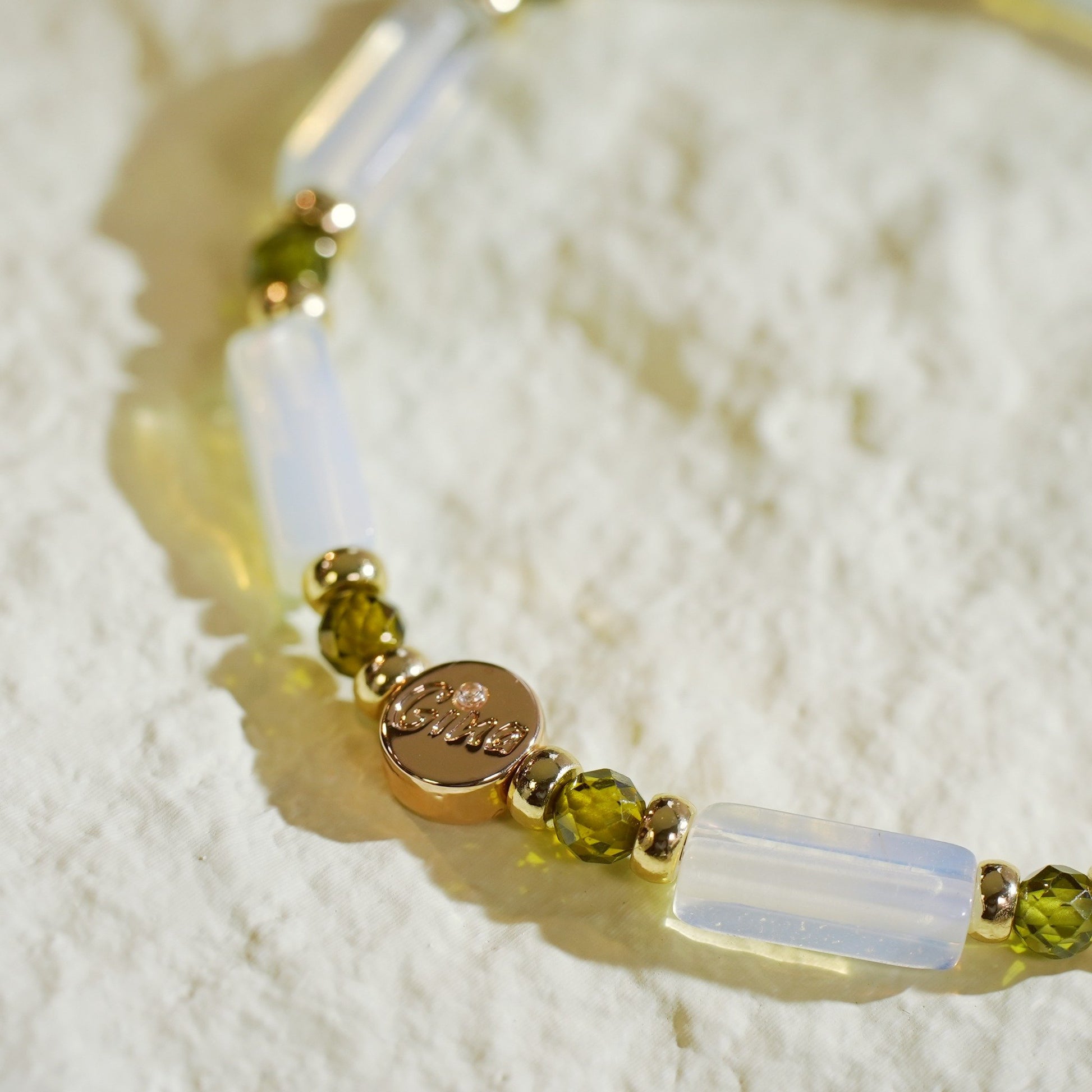 A unisex moonstone stretch bracelet with rectangular beads, deep green CZ accents, and gold-toned details. Designed by Gina Kim, symbolizing calm and quiet luxury