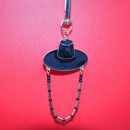 Black Korean hat motif key ring against a red background showing K POP shadow style inspired by JINU.