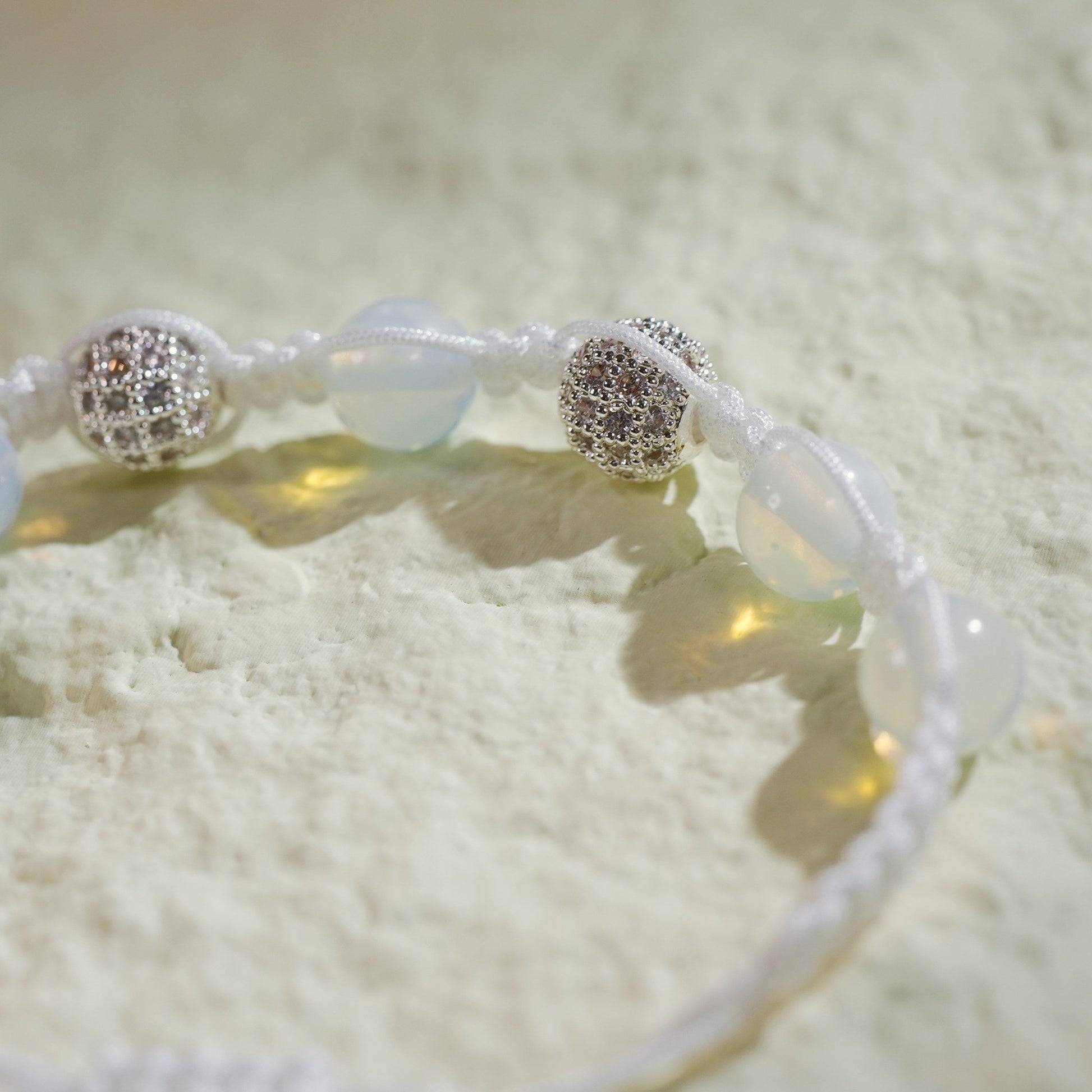 A handmade moonstone bracelet with silver-toned accents, featuring a soft glow and adjustable macramé closure with Gina Kim charm.