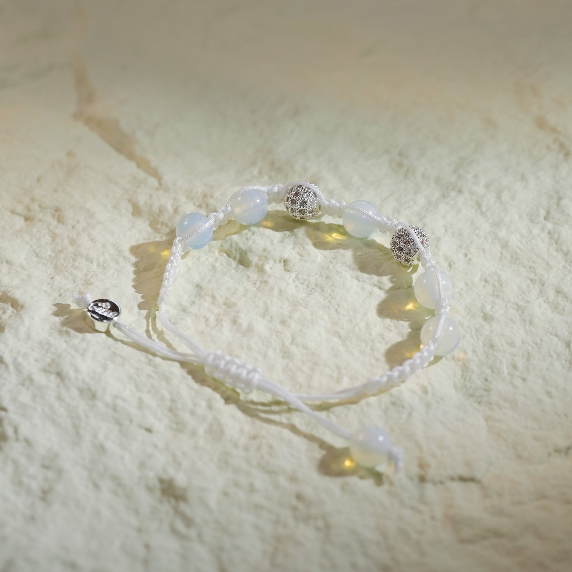 A handmade moonstone bracelet with silver-toned accents, featuring a soft glow and adjustable macramé closure with Gina Kim charm.