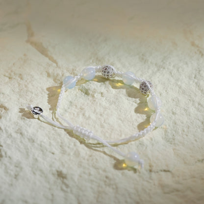 A handmade moonstone bracelet with silver-toned accents, featuring a soft glow and adjustable macramé closure with Gina Kim charm.