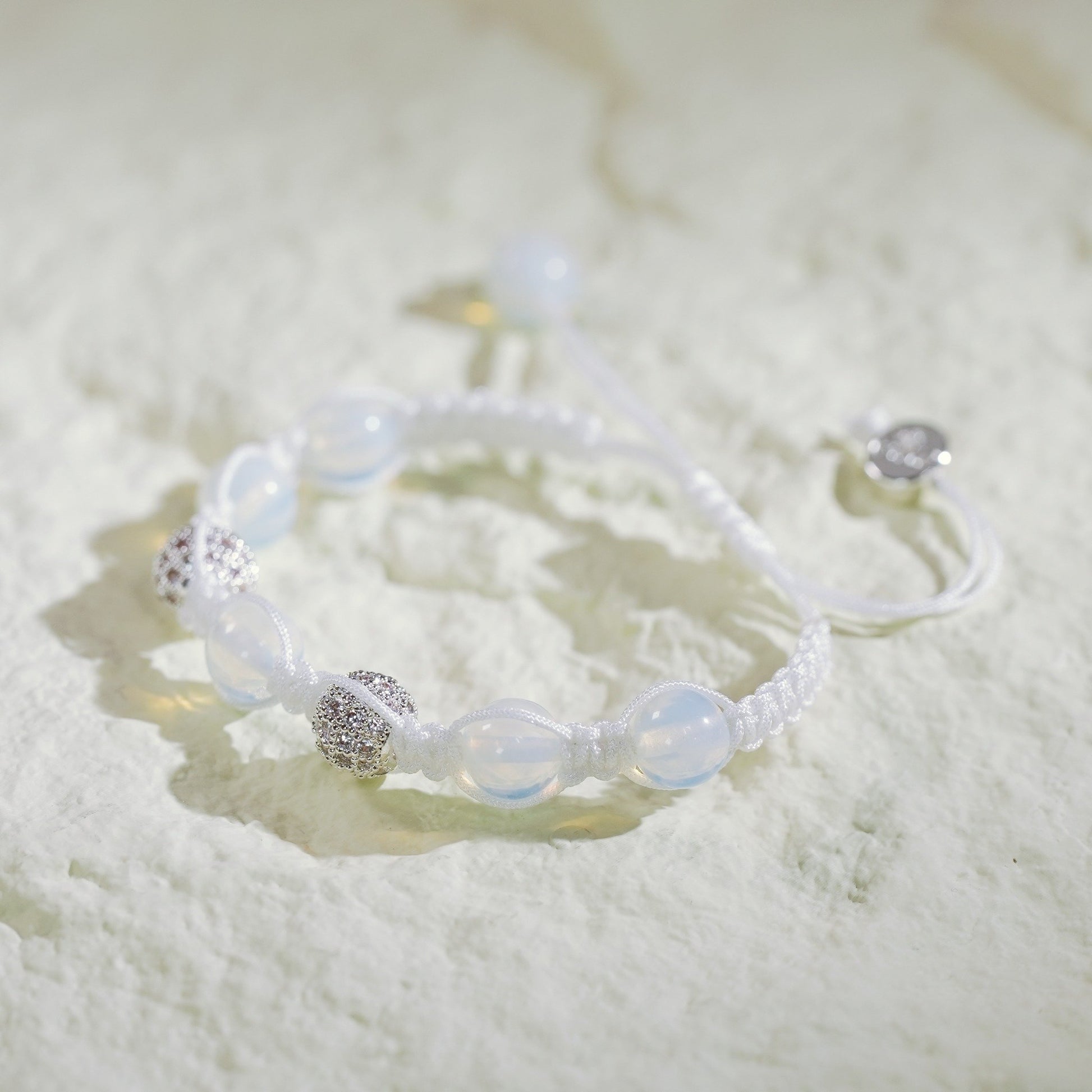 A handmade moonstone bracelet with silver-toned accents, featuring a soft glow and adjustable macramé closure with Gina Kim charm.