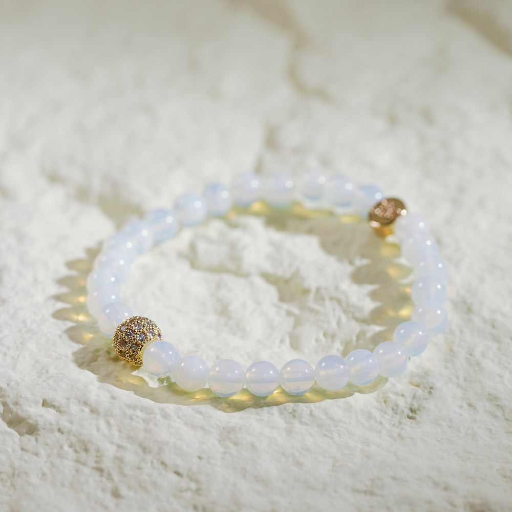 A stretch bracelet made with soft moonstone beads, a gold-plated CZ accent, and a GinaKimKR logo charm. Elegant and serene.