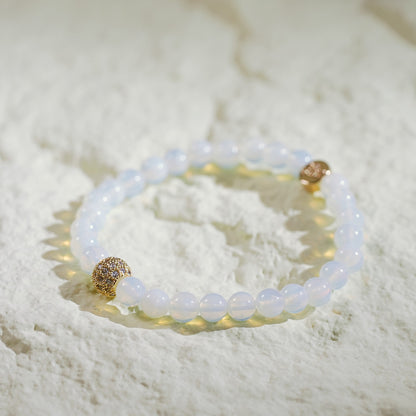 A stretch bracelet made with soft moonstone beads, a gold-plated CZ accent, and a GinaKimKR logo charm. Elegant and serene.
