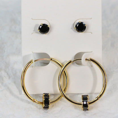 Front-facing image of Noir Balance Earring Set, with symmetric alignment of 6mm black CZ studs and crystal-accented gold hoops on a soft card.
