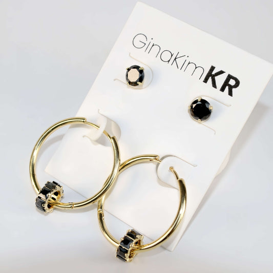 Angled close-up of Noir Balance Earring Set showing gold hoops with jet crystal detail and bold black CZ studs on a cream-toned product card.