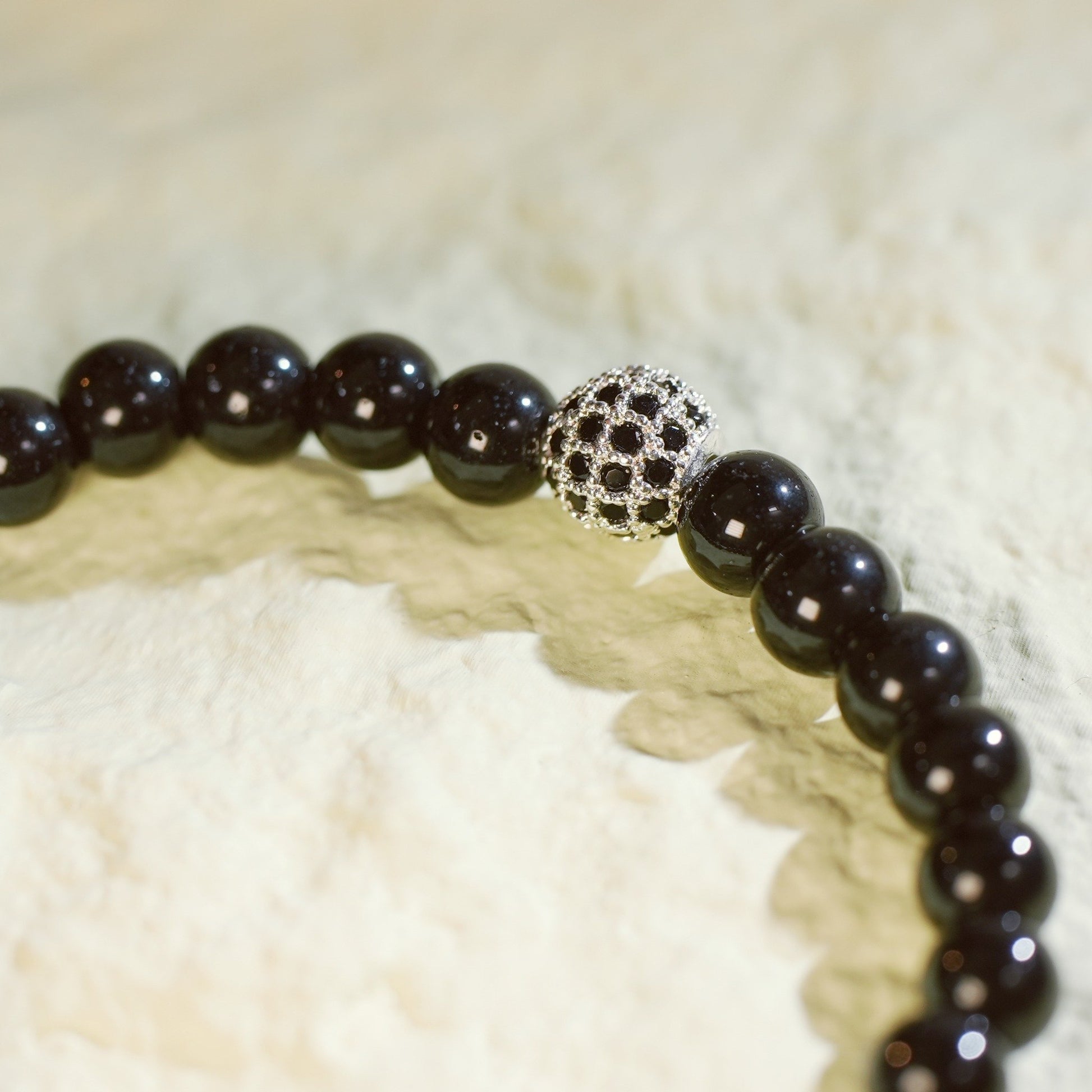 A stretch bracelet made with smooth black onyx beads, a silver-plated CZ accent, and Gina Kim logo charm. Bold and grounding.