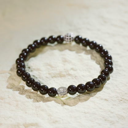 A stretch bracelet made with smooth black onyx beads, a silver-plated CZ accent, and Gina Kim logo charm. Bold and grounding