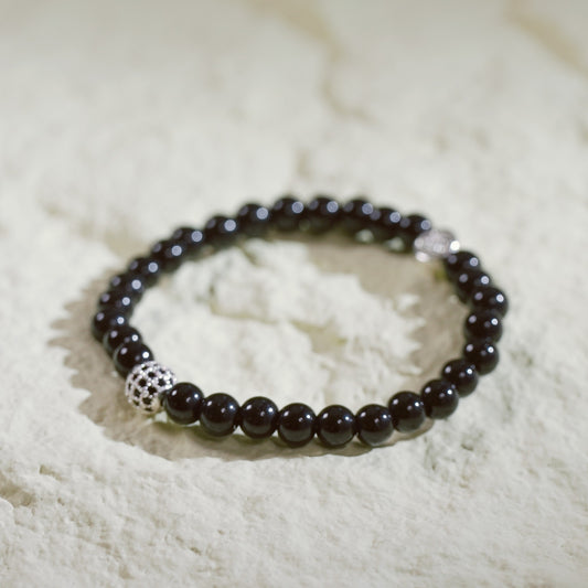 A stretch bracelet made with smooth black onyx beads, a silver-plated CZ accent, and Gina Kim logo charm. Bold and grounding.