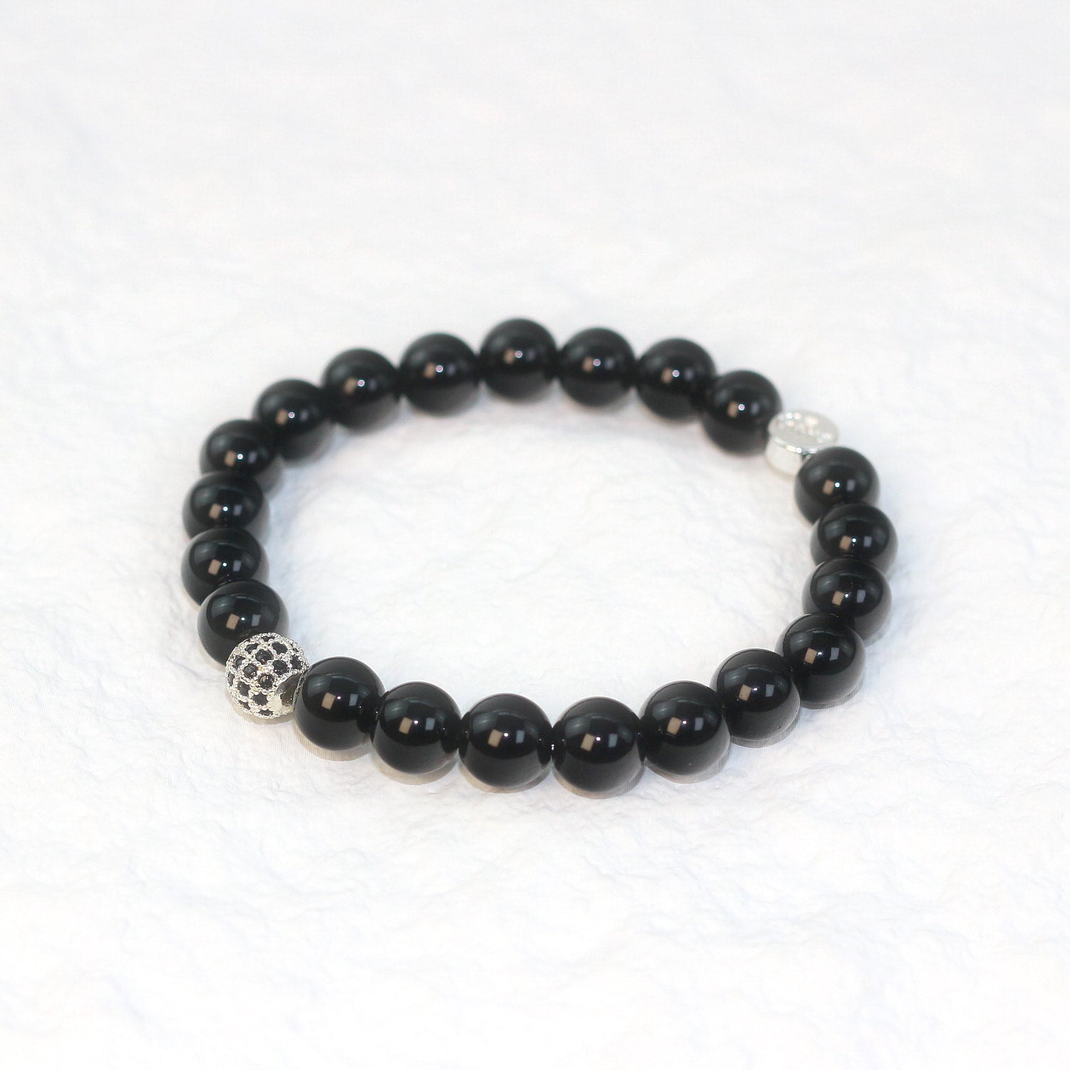 Top-down image of the Onyx Strength Bracelet featuring polished 8mm jet-black beads arranged in a circle on a clean white background.