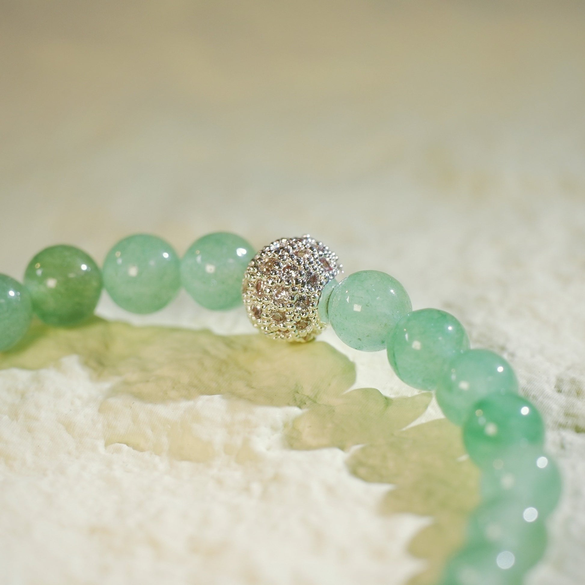 A stretch bracelet made with light green peridot beads, a gold CZ accent, and a Gina Kim logo charm. Bright, fresh, and handmade.