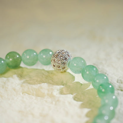 A stretch bracelet made with light green peridot beads, a gold CZ accent, and a Gina Kim logo charm. Bright, fresh, and handmade.
