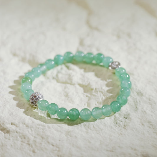 A stretch bracelet made with light green peridot beads, a gold CZ accent, and a Gina Kim logo charm. Bright, fresh, and handmade.