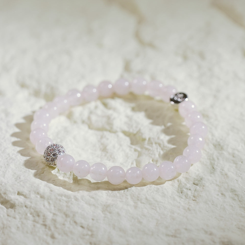 A stretch bracelet with soft pink rose quartz beads, gold CZ accent, and Gina Kim logo charm. Delicate and elegant.
