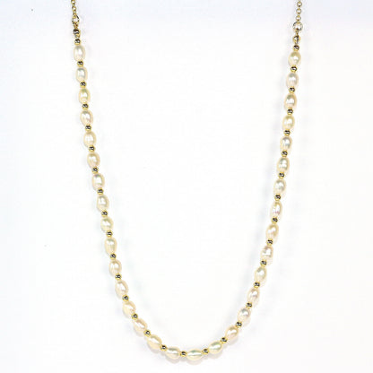 A flat lay photo of the Serenity Pearl Necklace by Gina Kim, featuring natural freshwater pearls and gold-tone accents, styled on ivory satin fabric for a luxurious and elegant look