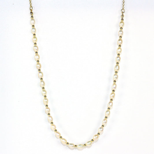 A flat lay photo of the Serenity Pearl Necklace by Gina Kim, featuring natural freshwater pearls and gold-tone accents, styled on ivory satin fabric for a luxurious and elegant look