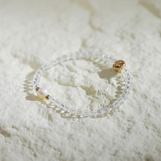 A stretch bracelet made with crystal quartz beads and a single freshwater pearl, accented with gold spacers and a GinaKimKR logo charm. Clean, soft, and handmade.