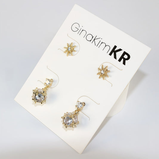 Top view of Starlume Earring Set with gold star studs and dimensional drop earrings, arranged on white card.