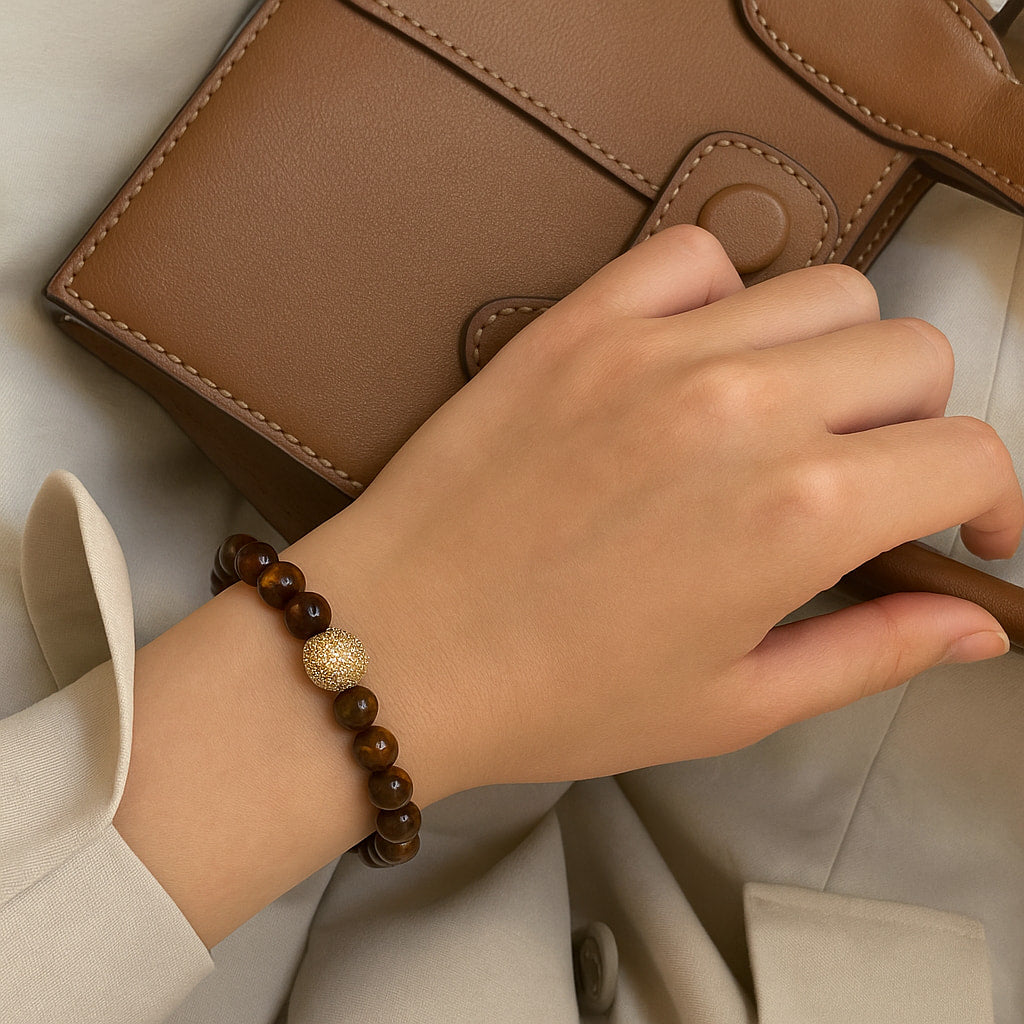 A person wearing the Tiger’s Eye Fortune Bracelet by Gina Kim, featuring shimmering golden-brown stones and gold accents. Strong and stylish.