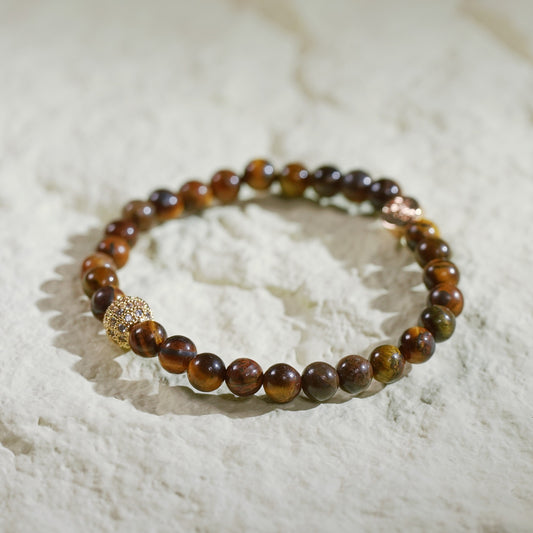 A stretch bracelet made with golden-brown tiger’s eye beads, gold-plated CZ accent, and Gina Kim logo charm. Grounding and empowering