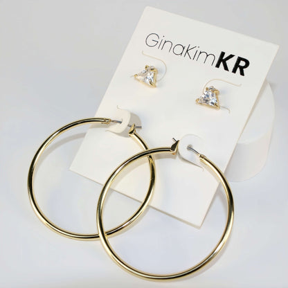 Triad Glow Earring Set shown in diffused daylight with triangle CZ studs and bold 42mm gold hoops, arranged on a soft cream product card.